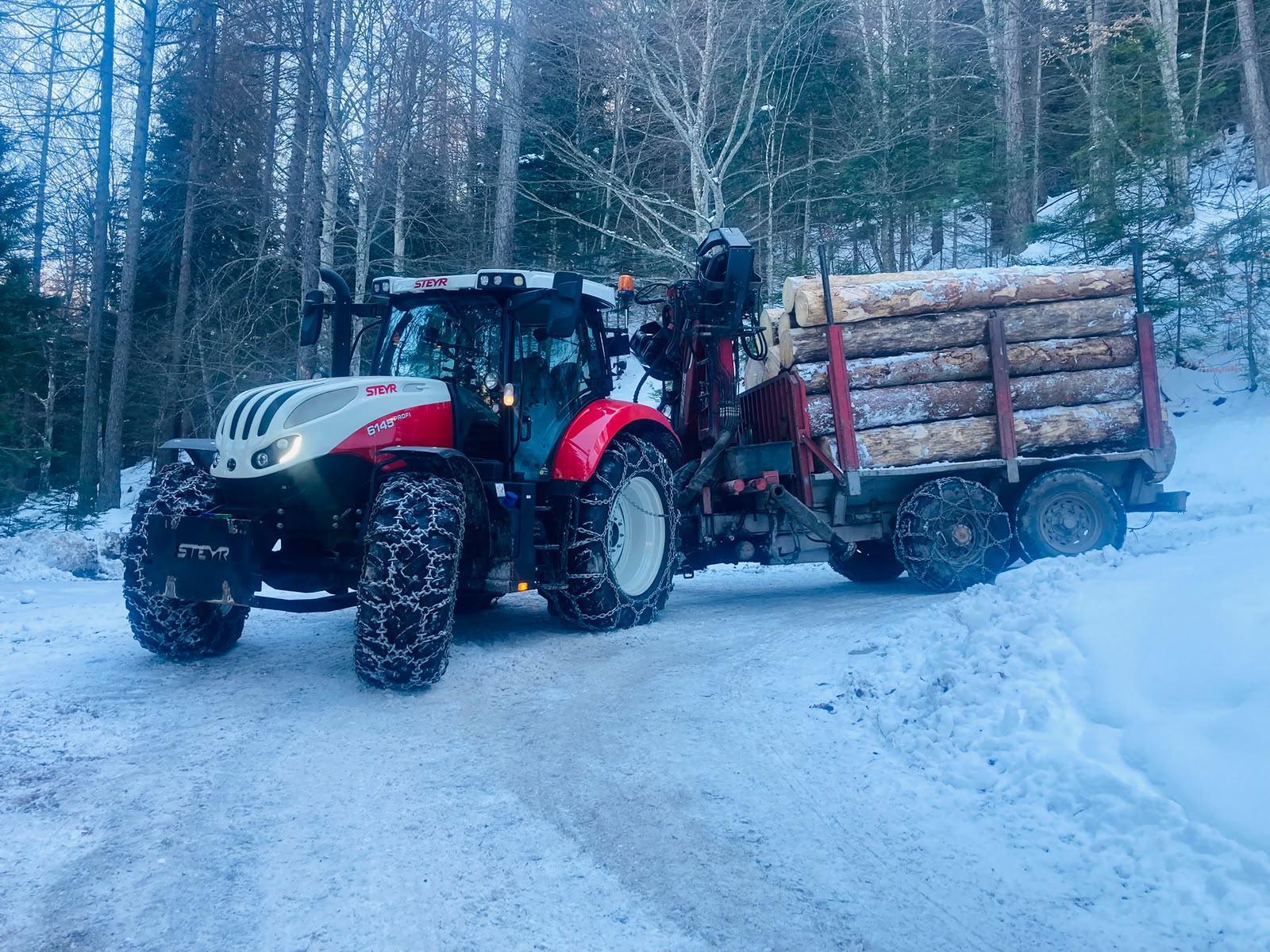 Trattore con catene e carico di tronchi su una strada innevata